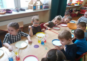 dzieci siedzą przy stolikach a talerze wypełnione są mlekiem